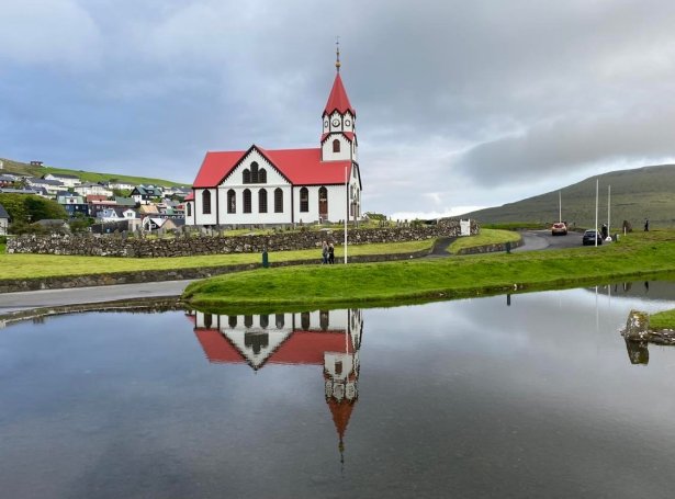 Sandavágs kirkja og húsini í bygdini við spegling í ánni, sædd frá vegarsíðuni